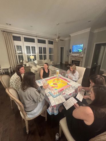 A group of women playing a board game around a table in a cozy living room.