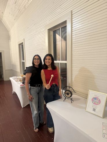 Two women smiling next to a table with a gong and a welcome sign.