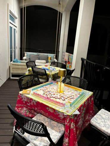 Cozy balcony setup with floral tablecloths and game boards under warm lamps.