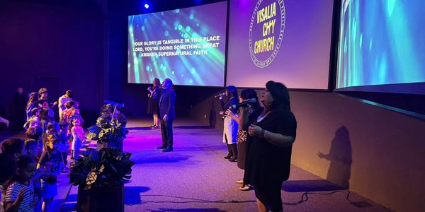 People worship and sing on stage at Visalia City Church with projected lyrics.