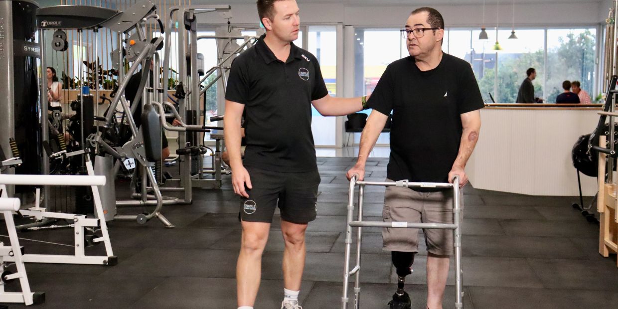 Clinician support older man with walking frame to walk through gym