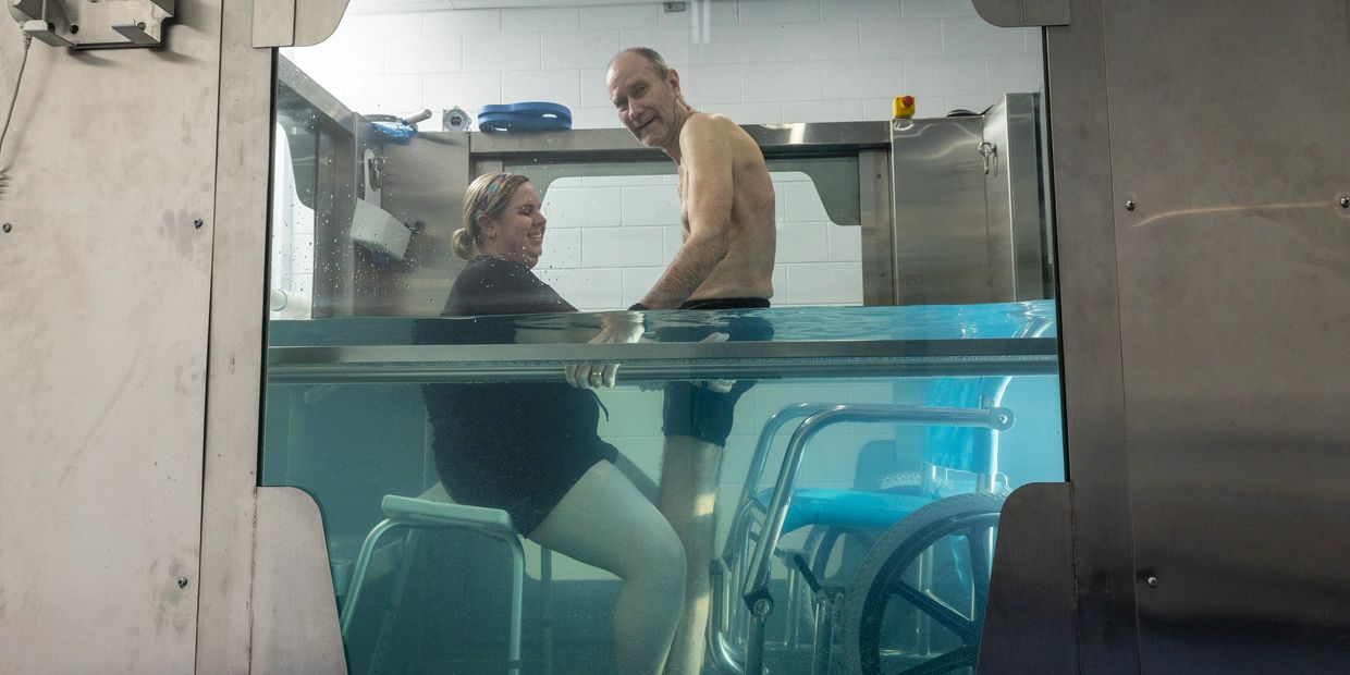 Older person standing in hydrotherapy tank with physiotherapist