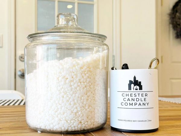 an apothecary jar filled with soy wax pellets next to a chester candle company tube