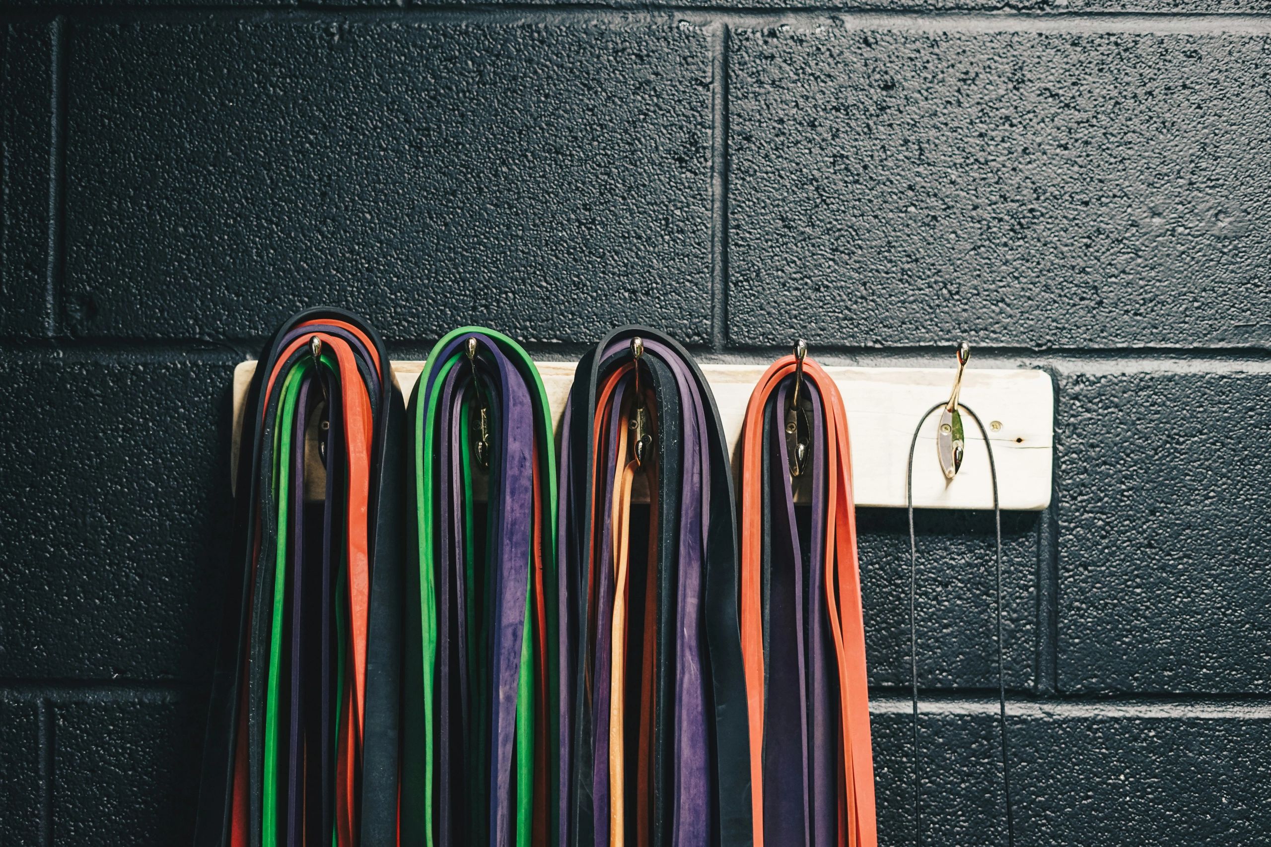 Colorful resistance bands hanging on hooks against a black wall.