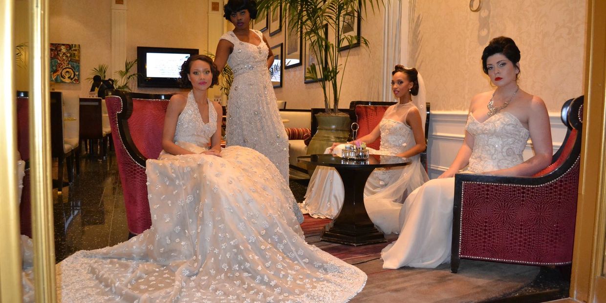 Four women in elegant white bridal gowns posing indoors on red chairs.