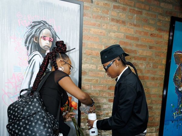 Two people interacting near artwork on a brick wall indoors.