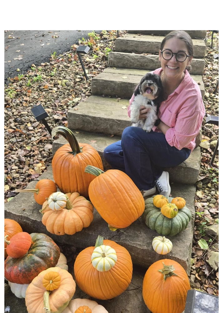 Woman in glasses holding a small dog surrounded by various pumpkins on stone steps. Pumpkin display delivered Fairfax Virginia