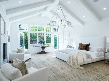 Bright bedroom with white furniture and large windows overlooking greenery.