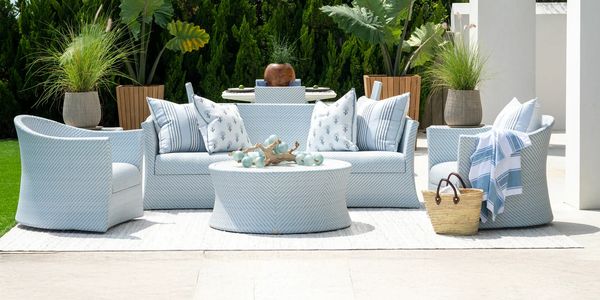 Cozy outdoor seating area with light blue cushions and tropical plants.
