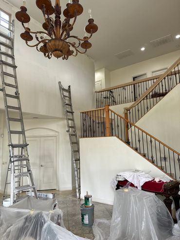 Interior of a home undergoing painting with ladders and furniture covered in plastic.