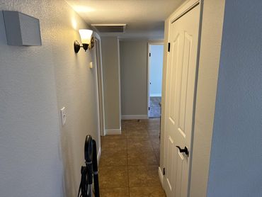 A hallway with tiled floor, white doors, and a vacuum cleaner leaning against the wall.