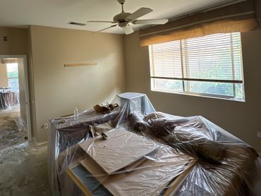 Room with furniture covered in plastic sheets during renovation.