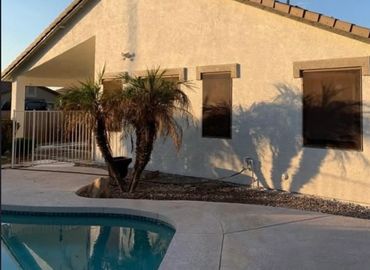A sunny house exterior with palm trees casting shadows and a pool in front.