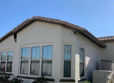 Modern single-story house with beige walls and a tiled roof under a clear blue sky.