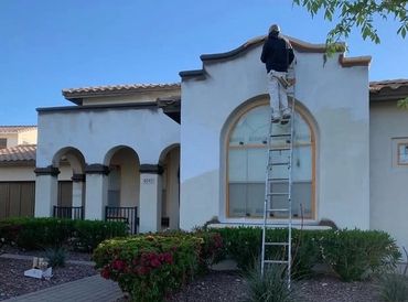 A person on a ladder painting a house exterior under clear blue sky.