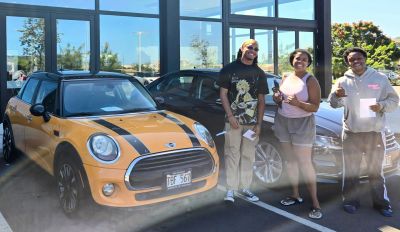 Three people posing by their new Mini Cooper car in Hawaii.