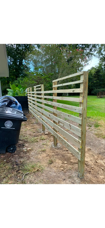 Newly built wooden fence with horizontal slats beside a trash bin.
