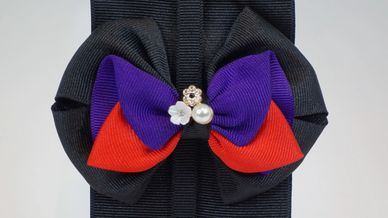 Decorative bow with black, purple, and red ribbons accented by small flower and pearl embellishments.
