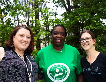 Three women smiling outdoors with greenery in the background.