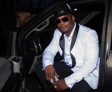 Man dressed in a white tuxedo jacket sitting in a car at night.