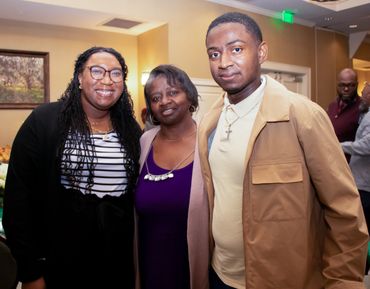 Three people smiling together at an indoor event in a warmly lit room.
