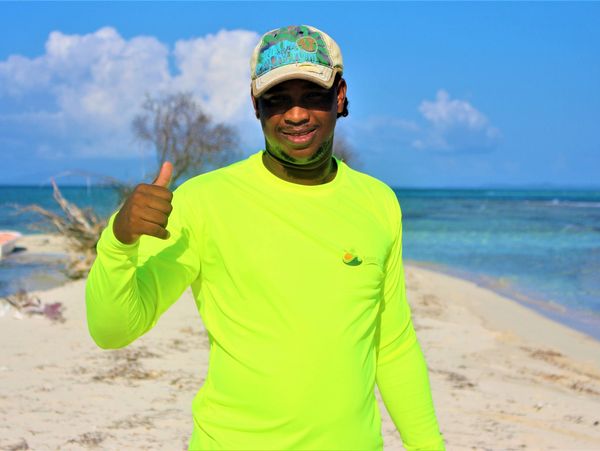 Man in neon green shirt giving thumbs up on a sunny beach.