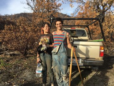 A young smiling couple in work clothes hold tree planting tools. 