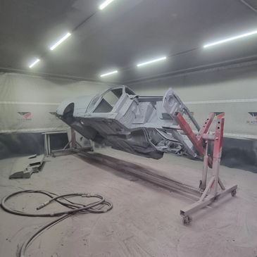 Car body frame suspended on a rotisserie in a workshop.