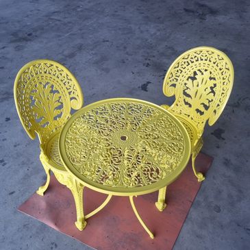 Yellow ornate metal table with two matching chairs on a concrete floor.
