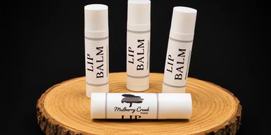 Four white lip balm tubes displayed on a wooden slab against a black background.