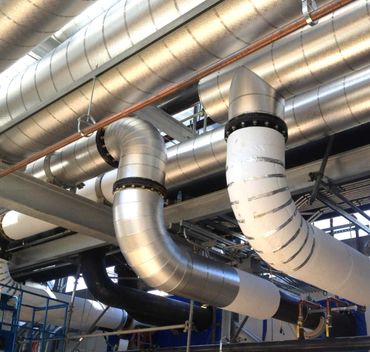 Large metallic and insulated pipes in an industrial facility ceiling.