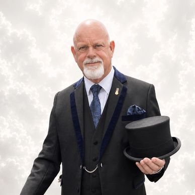 Elderly man in formal attire holding a black top hat.