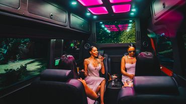 Four women enjoying a luxurious ride with neon pink ceiling lights.