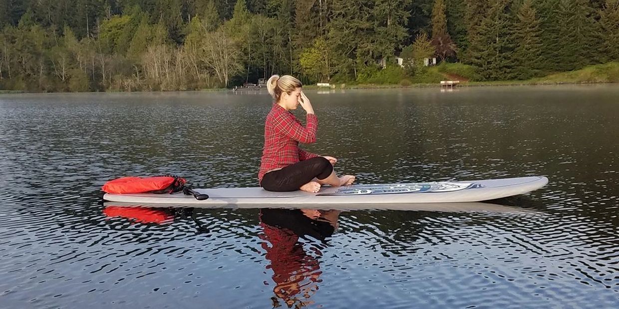 Person meditating on a paddleboard in calm water.