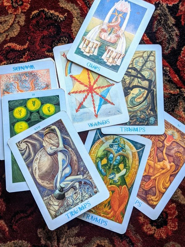 A spread of illustrated tarot cards on a patterned carpet.
