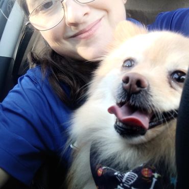 Smiling person taking a selfie with a happy dog wearing a festive bandana.