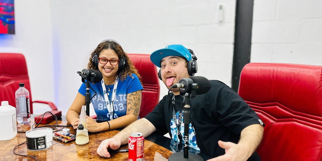 Two people recording a podcast, one smiling and the other playfully sticking out his tongue.