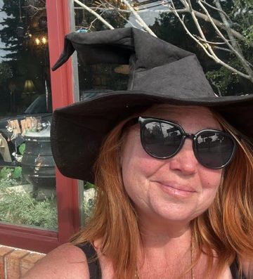 Woman wearing a witch hat and sunglasses smiling.