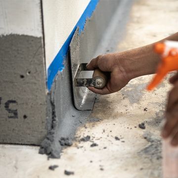 Hand smoothing wet cement on a wall corner.