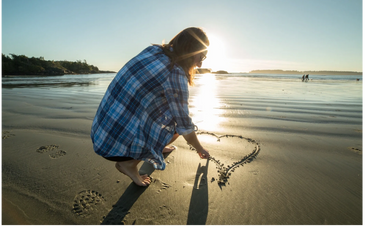 Woman drawing a heart on the beach at sunset.