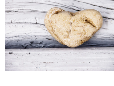 A heart-shaped beige stone resting on a textured white wooden surface.