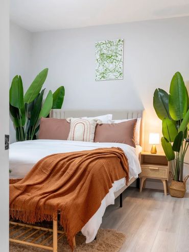 Cozy bedroom with white bedding, rust throw blanket, and green plants.