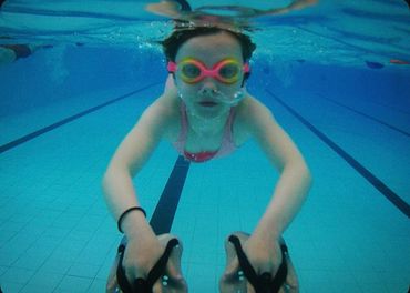 Child swimming underwater with goggles and kickboards in a pool.