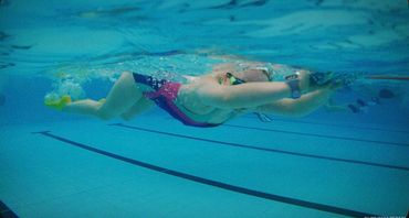 Person swimming underwater in a pool with goggles and swimwear.