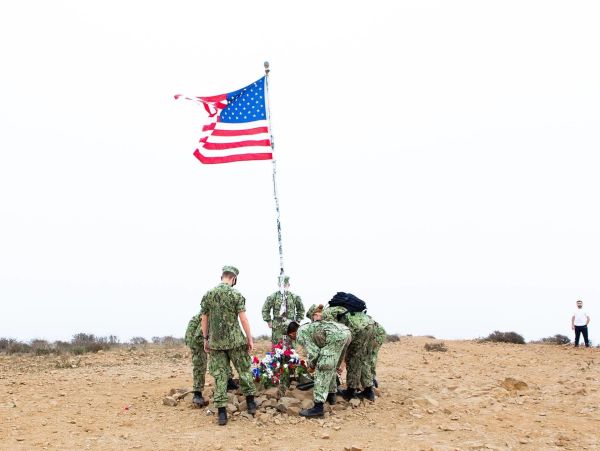Soldiers honoring flag and memorial outdoors.