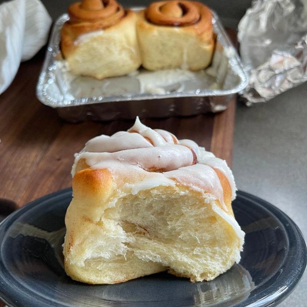 Bite taken out of iced cinnamon roll on plate.