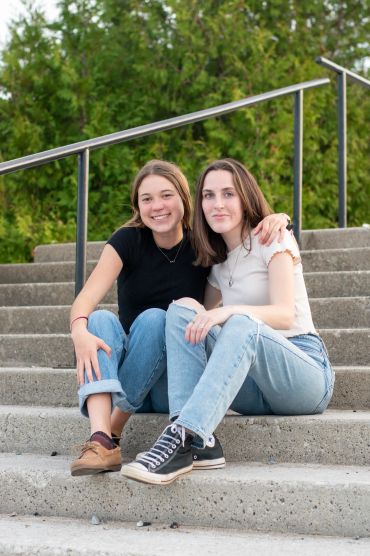 Two young women sitting on outdoor steps, smiling and posing together.