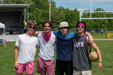 Four friends posing together on a sunny sports field.