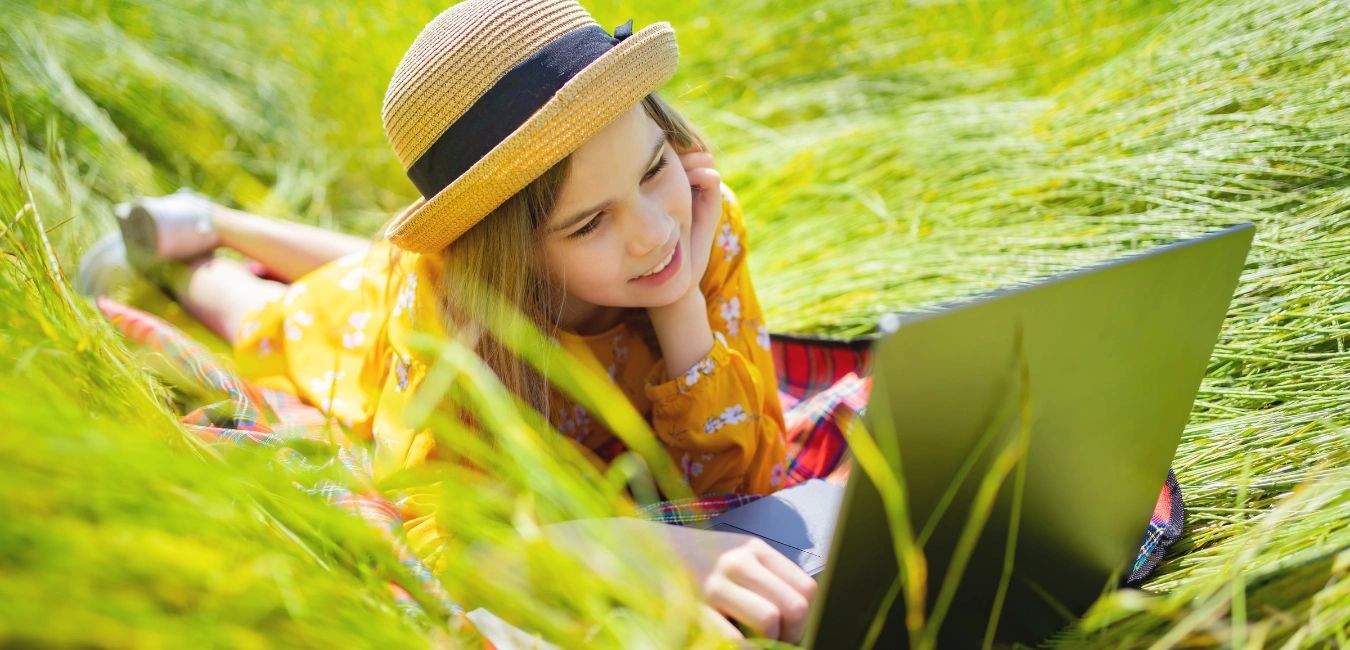 Young girl smiling while lying in the grass and looking at a computer