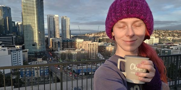 Woman in purple hat enjoys coffee on city balcony at sunset.